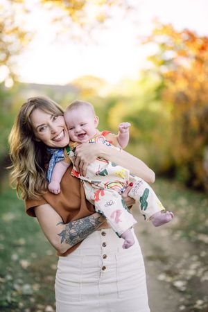 Mother and baby share joyful moments together during an autumn photoshoot in a sunlit outdoor setting.