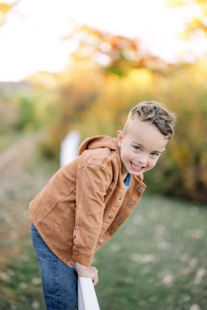 A playful portrait of a child in a brown jacket against a blurred autumn background.