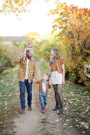 Family walking together on an autumn path surrounded by golden fall foliage and scattered leaves on the ground.