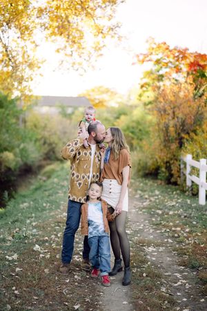 Family sharing tender moments together on an autumn path lined with colorful fall foliage and white fencing.