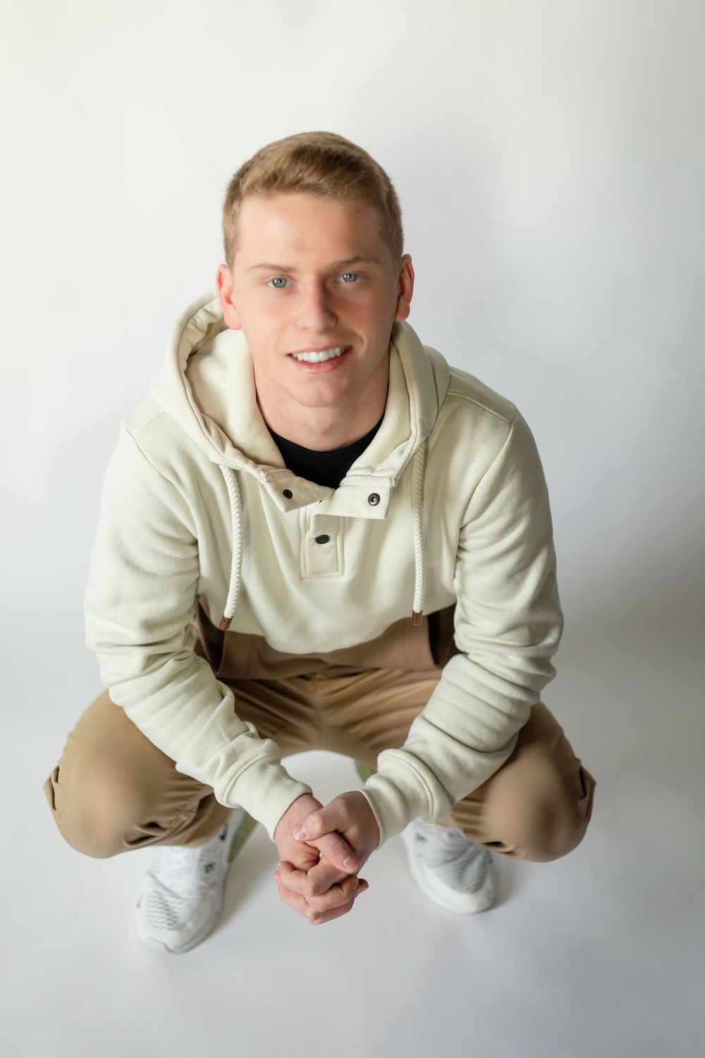 A person in a cream colored sweatshirt lies on their stomach in a playful pose against a white background.