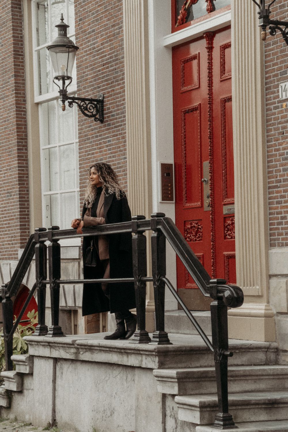Historic building entrance with red doors, white columns, and brick facade in Amsterdam.