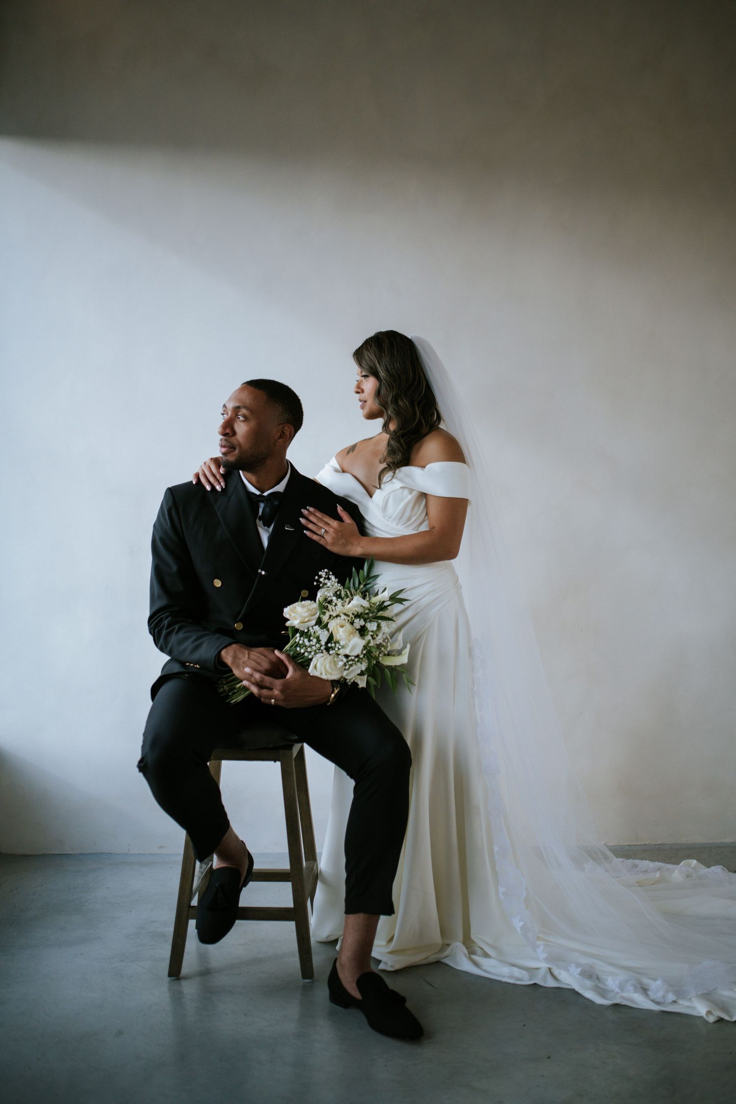 Elegant wedding portrait featuring a white gown and formal attire against a minimalist grey backdrop.