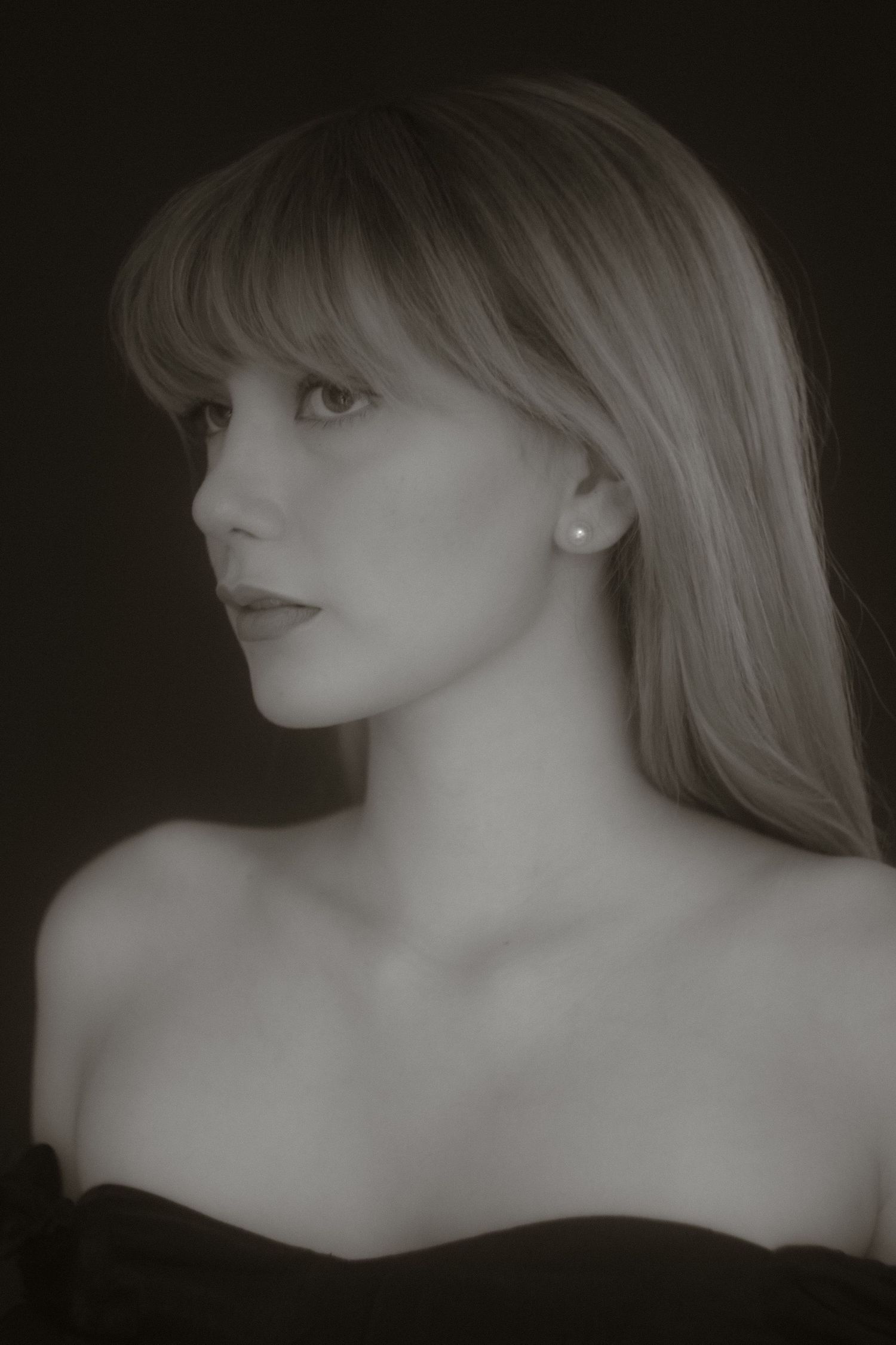 Classic black and white side portrait of blonde woman with bangs wearing off-shoulder top.