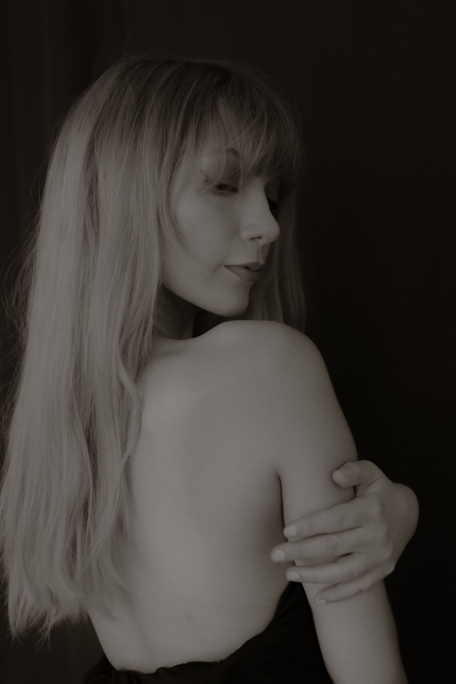 Black and white portrait of a blonde woman with bangs, bare shoulders, looking away.
