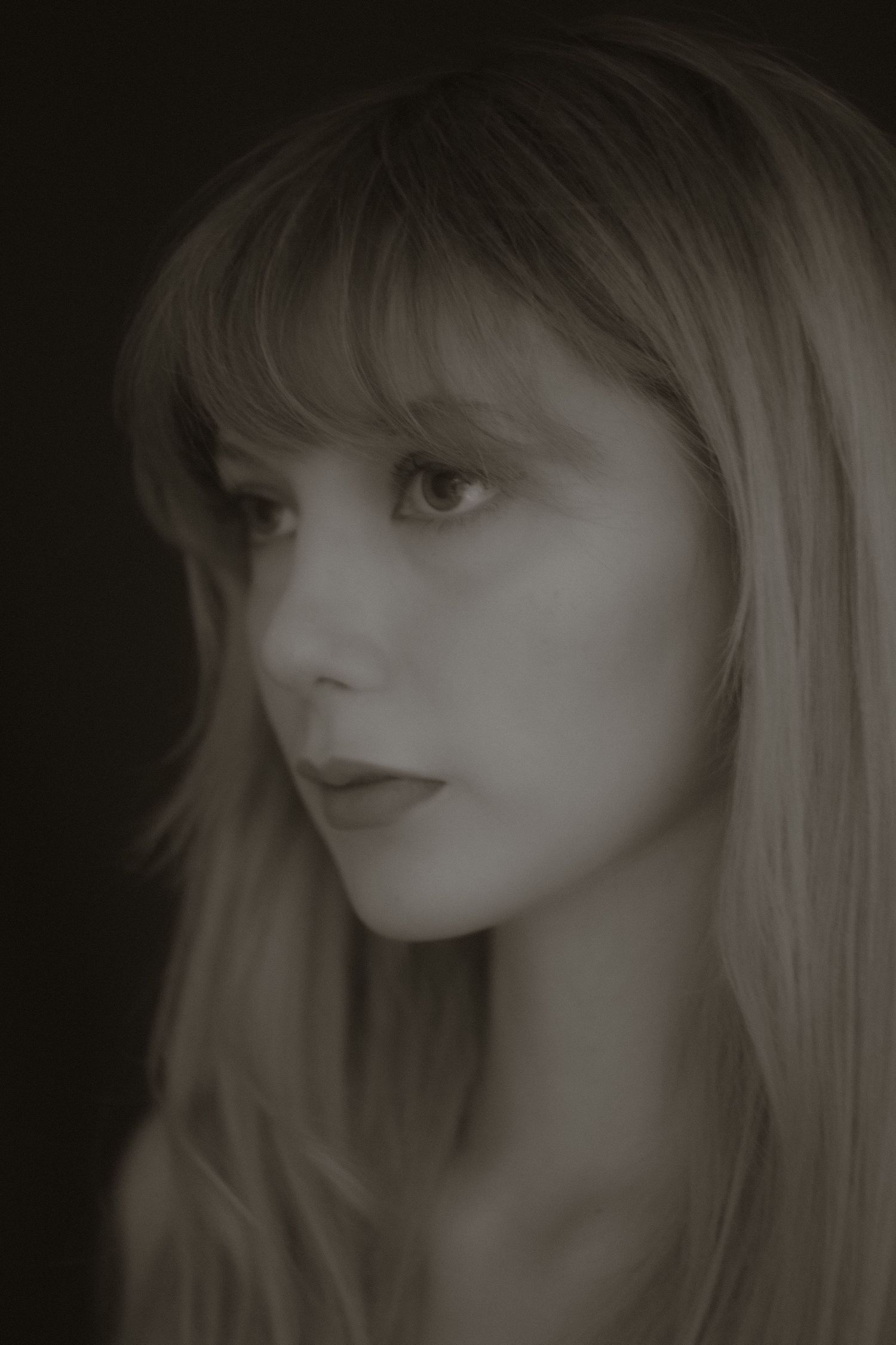Close-up monochrome portrait of a young blonde woman with bangs and dark lips.
