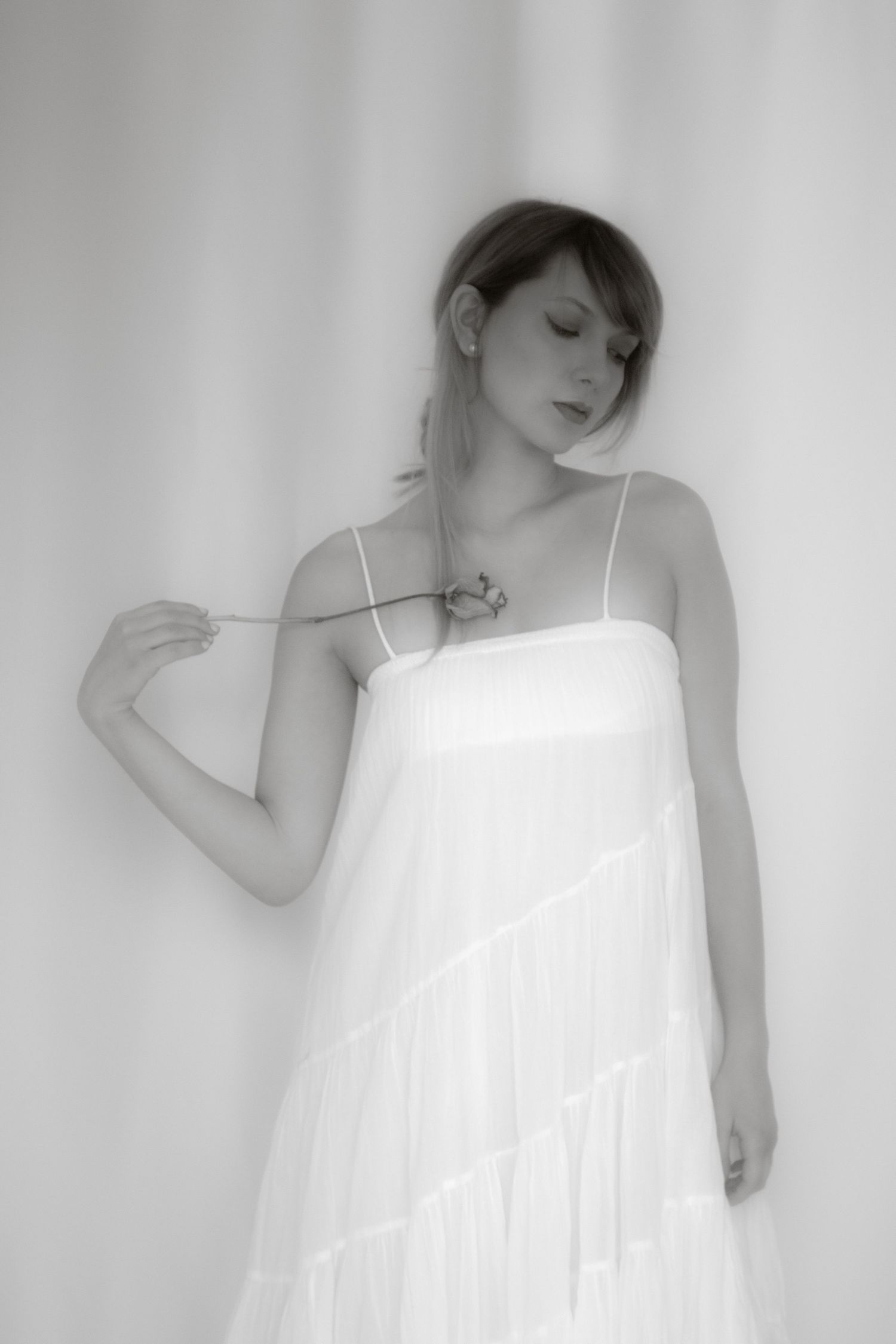 Soft black and white photo of a woman in a flowing white spaghetti strap dress.