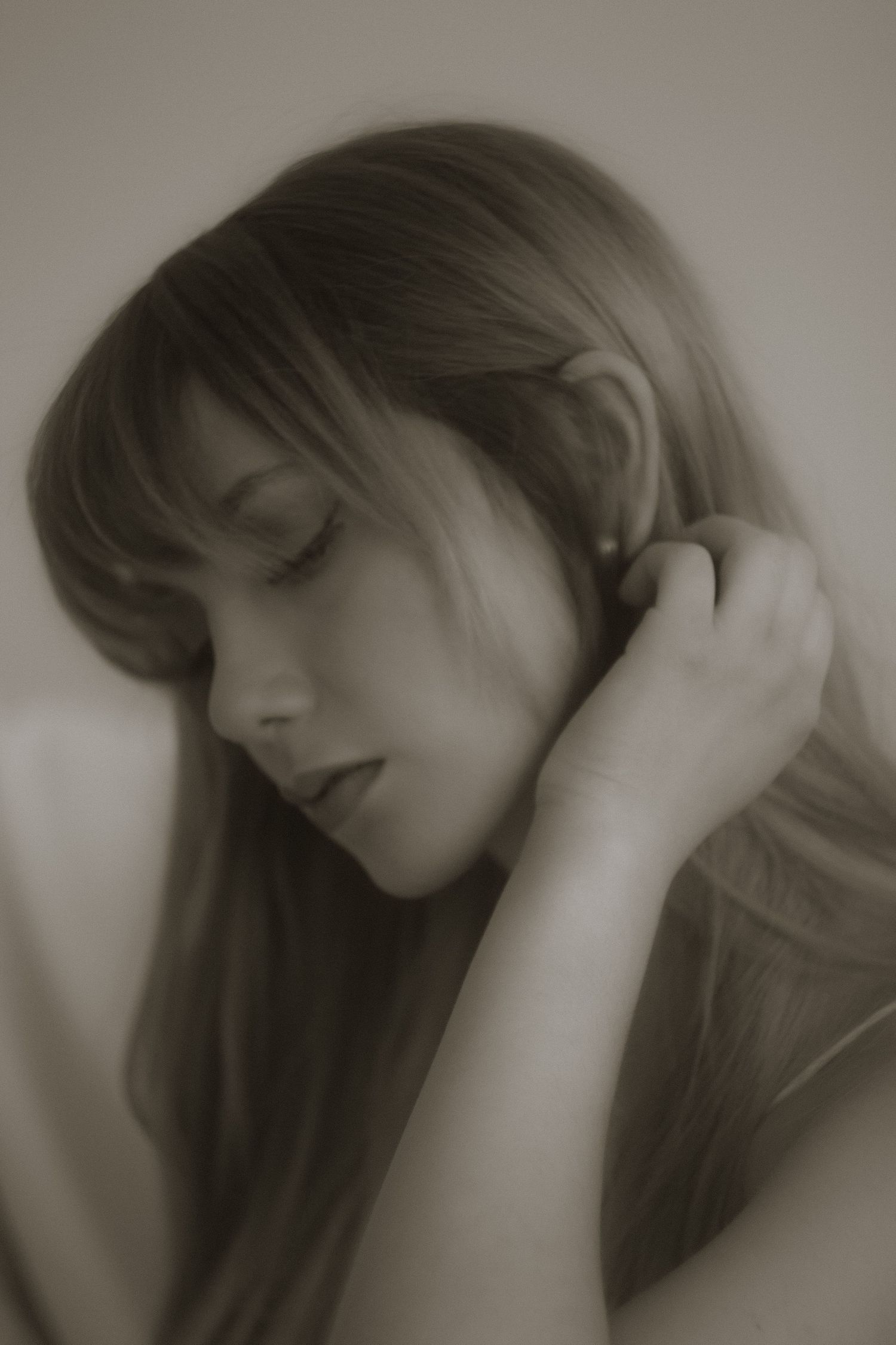 Dreamy sepia close-up of a woman with long hair gently touching her ear.