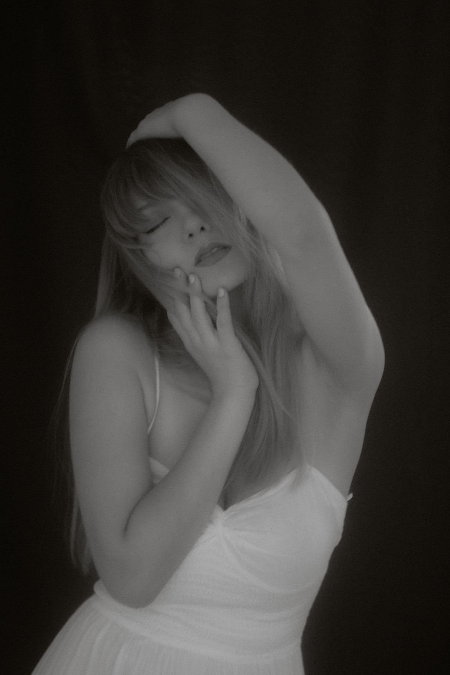 Black and white portrait of a woman in white dress with arm raised above head.