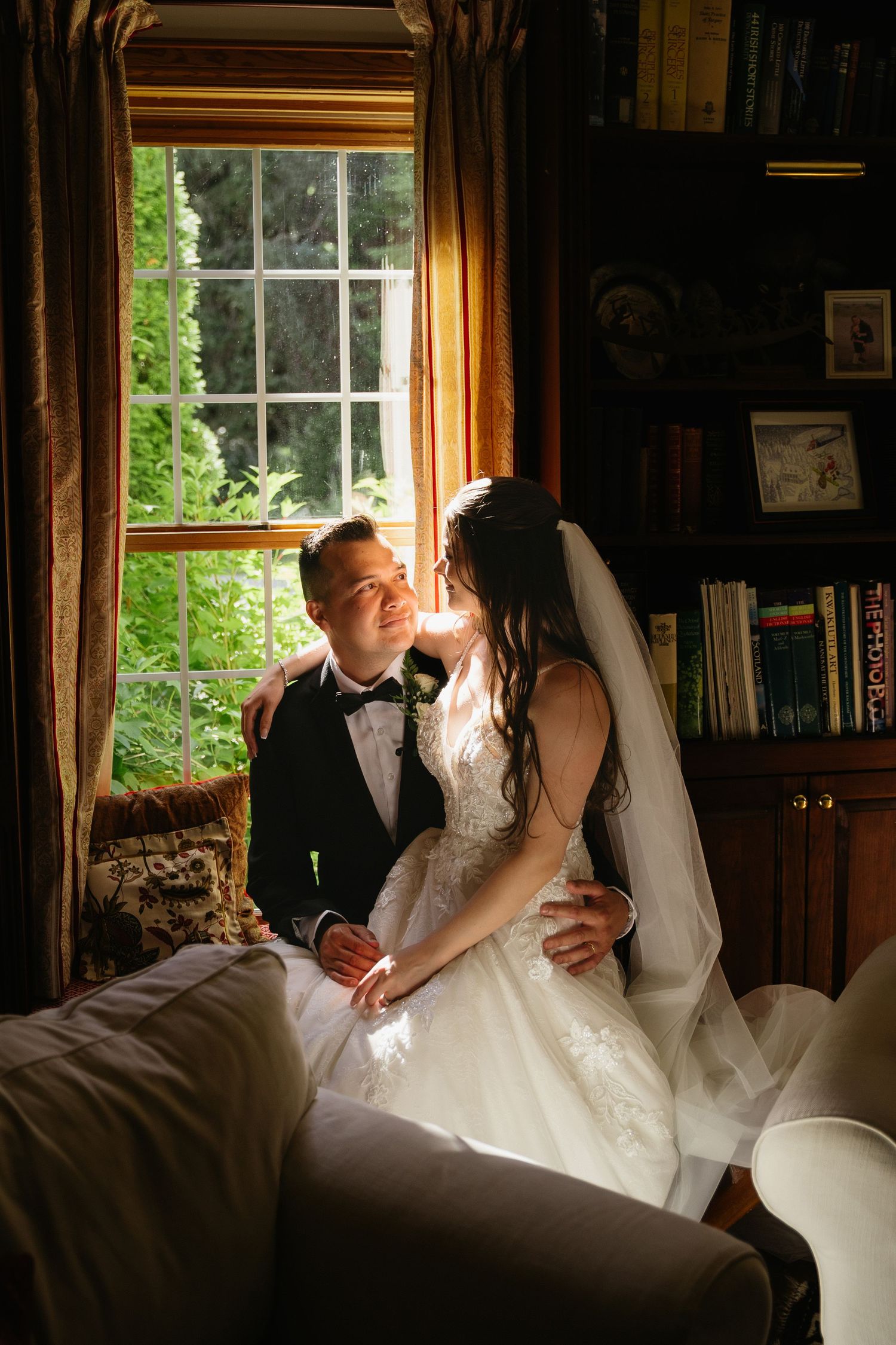 Romantic couple in formal attire embracing in dramatic lighting against wooden wall.