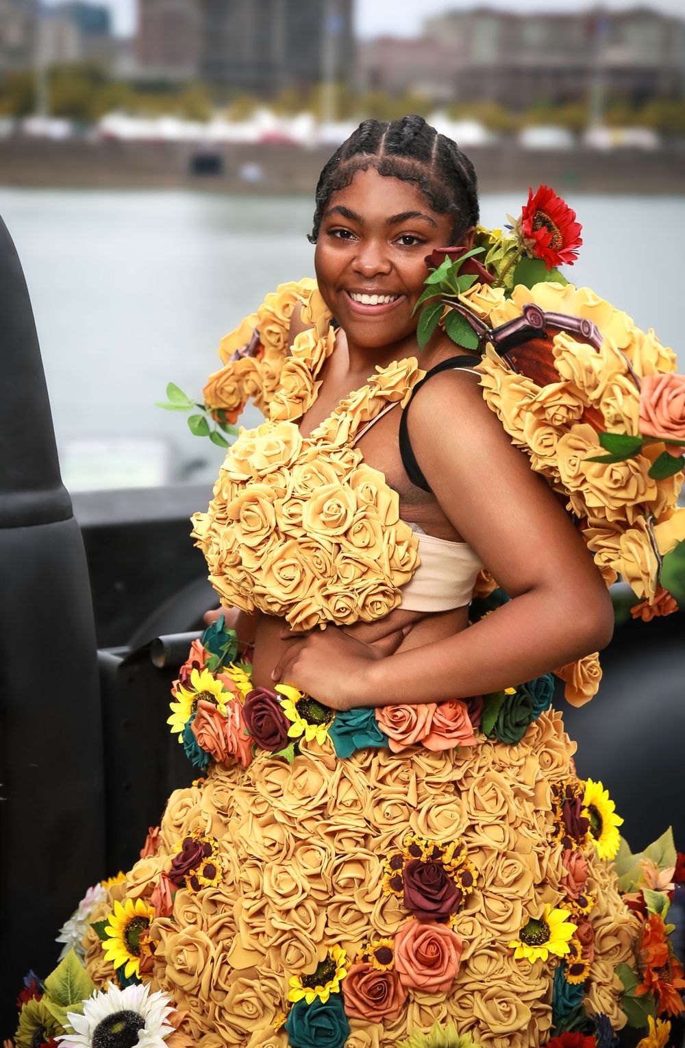 Someone wearing a stunning yellow ruffled dress adorned with colorful roses and sunflowers poses by the waterfront.