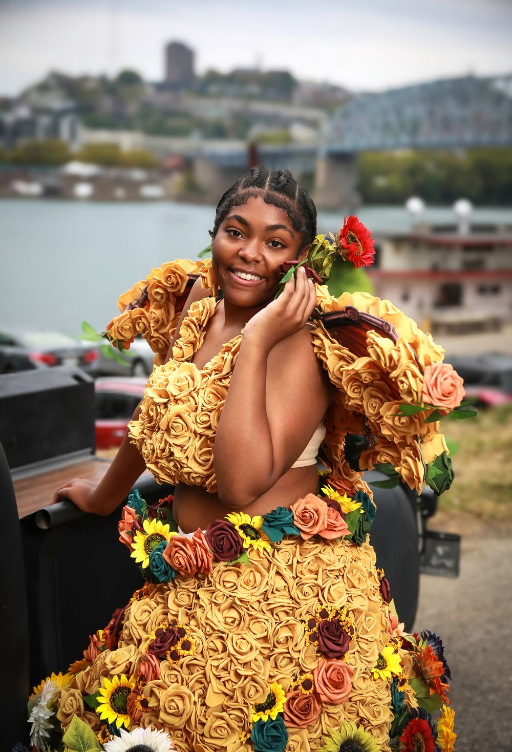 A person wearing a vibrant yellow ruffled dress adorned with colorful flowers poses by the waterfront.