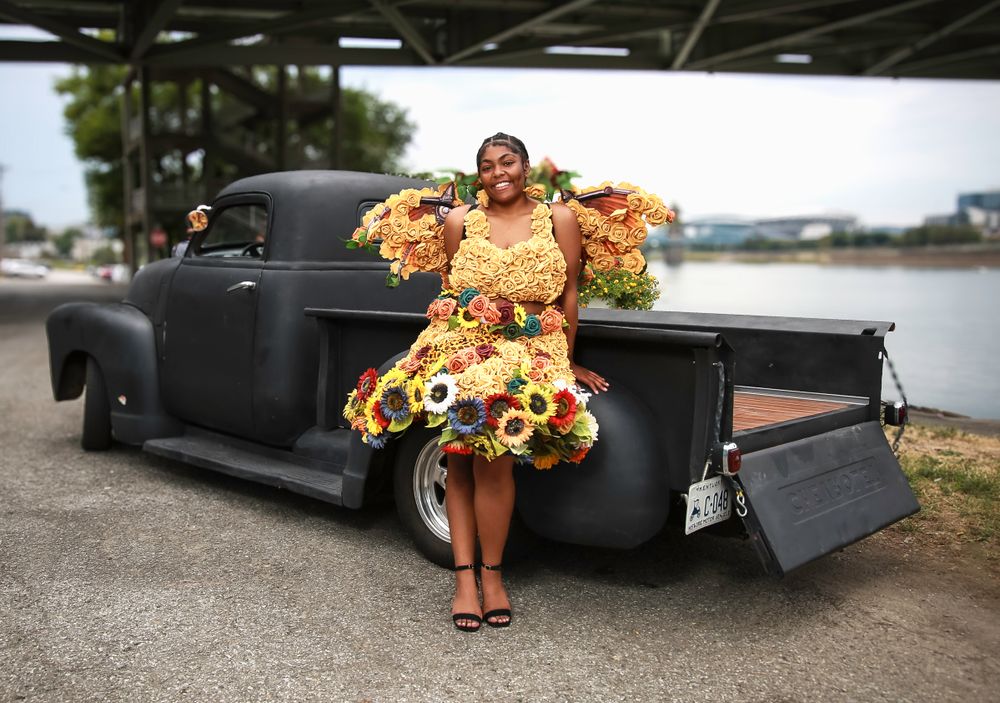 Vintage black pickup truck with person in bright floral dress posing by lowered tailgate in parking lot.