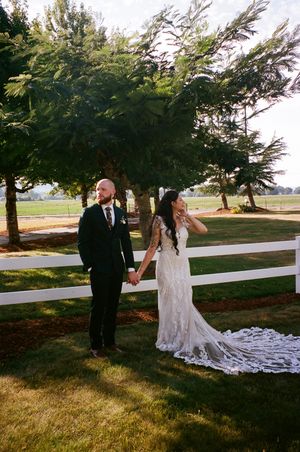 A wedding couple dances together in a scenic outdoor setting with trees and a white fence in the background.