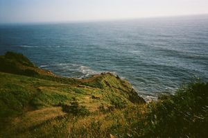Panoramic view of rugged coastal cliffs overlooking the vast blue Pacific Ocean on a sunny day.