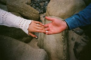 Two hands reaching towards each other against a dark textured background in a dramatic gesture.
