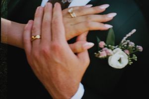 Hands with wedding rings and a delicate white floral boutonniere touch in an intimate wedding moment.
