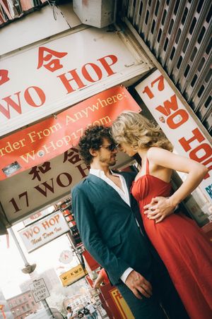 Couple kissing outside Wo Hop restaurant in NYC Chinatown, man in blue suit, woman in red dress.