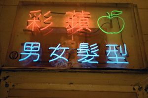 Colorful neon signs in Chinese characters with a green apple logo on a dark wall in an Asian hair salon.