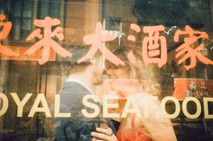 Couple sharing a romantic kiss reflected in a Royal Seafood restaurant window with Chinese characters.