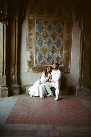 Couple in white outfits sitting together under ornate archway at Bethesda Terrace, Central Park.