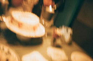 Blurred close-up of a glowing birthday cake with candles at a warm indoor celebration.
