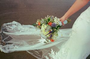 Bride holding a colorful wedding bouquet with her lace veil spread on the ground.
