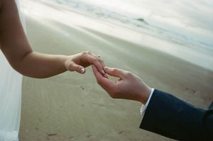 Couple exchanging wedding rings on a sandy beach during an outdoor ceremony.