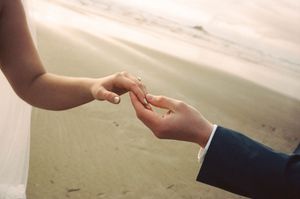 Bride and groom exchanging wedding rings on a sandy beach during golden hour.