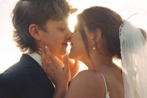 Bride and groom sharing a romantic kiss bathed in golden sunlight at their wedding.