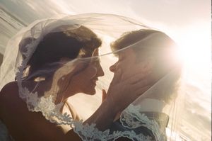 Romantic couple sharing an intimate moment under a lace bridal veil at sunset.