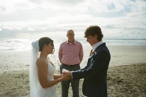 Couple exchanging vows during a romantic beach wedding ceremony with an officiant on a sandy shore.