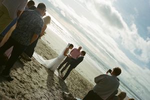 Guests gather on a sandy beach to witness an outdoor wedding ceremony with ocean waves in the background.