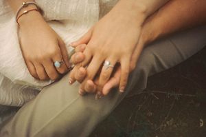 Close-up of a bride and groom holding hands, both wearing wedding rings, in an intimate moment.
