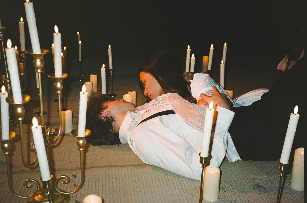 Two performers embrace dramatically among golden candelabras with lit white candles in a theatrical stage production.