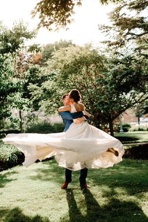 Couple spins in garden setting with flowing white dress catching sunlight.