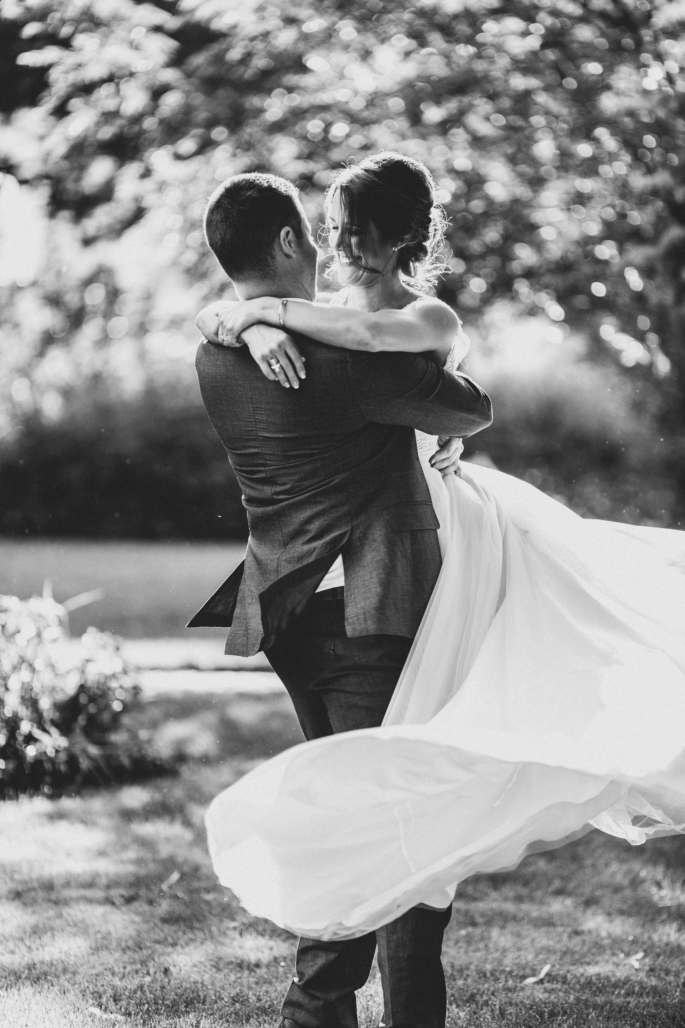 Black and white photo of newlyweds dancing outdoors with flowing white wedding dress.