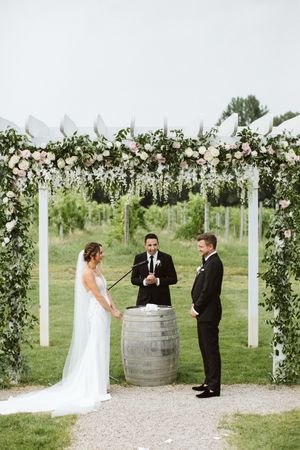 Wedding ceremony setup with floral archway and wine barrels in a vineyard setting.