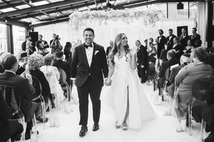 Wedding guests dance and celebrate at an indoor reception venue under industrial ceiling beams.