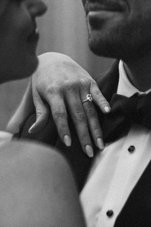Black and white detail shot of hands and formal wear at an elegant wedding.