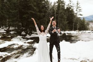 Joyful couple celebrates in snowy mountain setting with dramatic gestures.