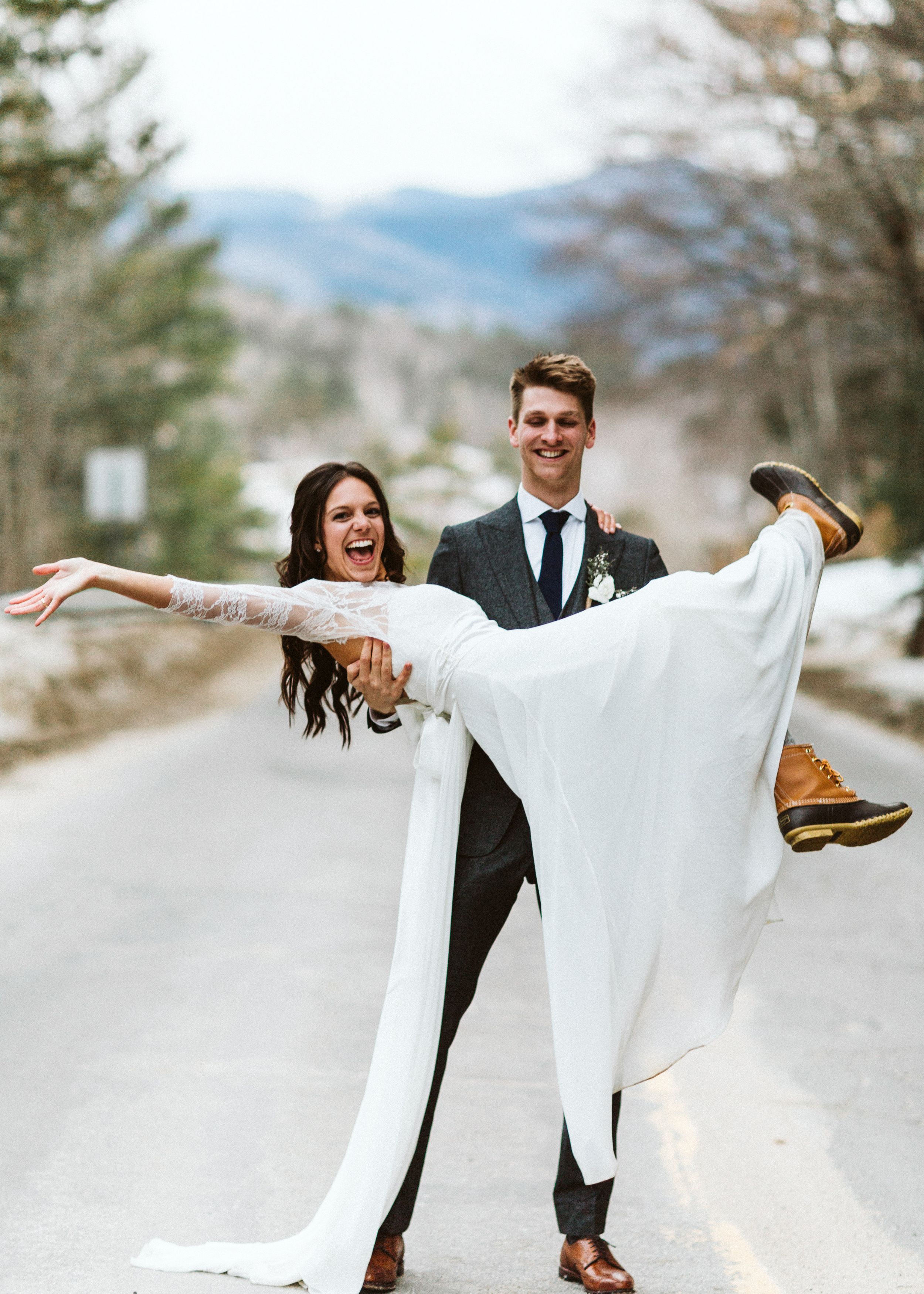 Playful wedding couple poses on mountain road with dramatic lift pose.