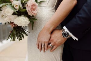 Wedding details showing bouquet of pink and white roses with hands holding flowers.