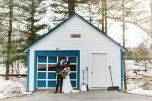 White cottage with blue trim and windows nestled among tall pine trees.