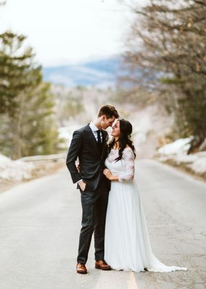 Newlyweds share an intimate moment on a snowy mountain road.