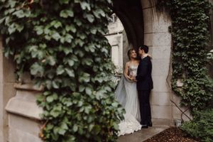Romantic wedding couple embracing against an ivy-covered stone wall backdrop.