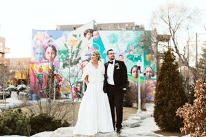 A couple poses in front of a vibrant street art mural on their wedding day.