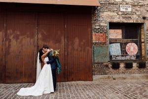 Wedding couple poses against rustic brick wall and industrial metal doors.