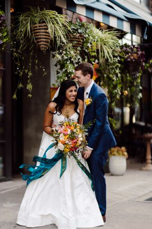 Couple in wedding attire embracing outdoors with lush greenery and plants in the background.