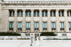 Wedding couple stands in front of a grand neoclassical building with columns.